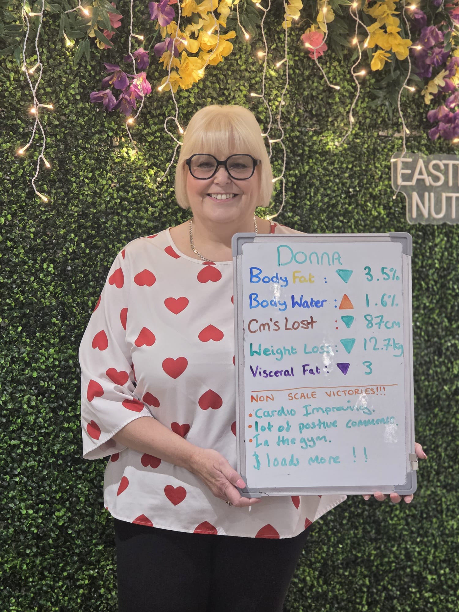 Donna smiling at Eastbourne Nutrition and holding her review board showing 12.7 kg lost and 87 cm lost